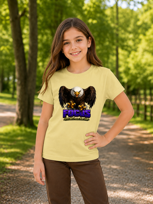 Young girl wearing a yellow t-shirt with an eagle graphic and 'FOCUS' text in a forest setting